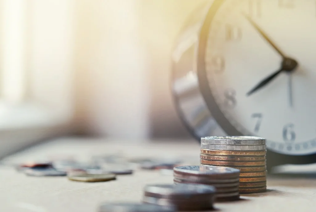 Stacks of coins in front of an alarm clock.