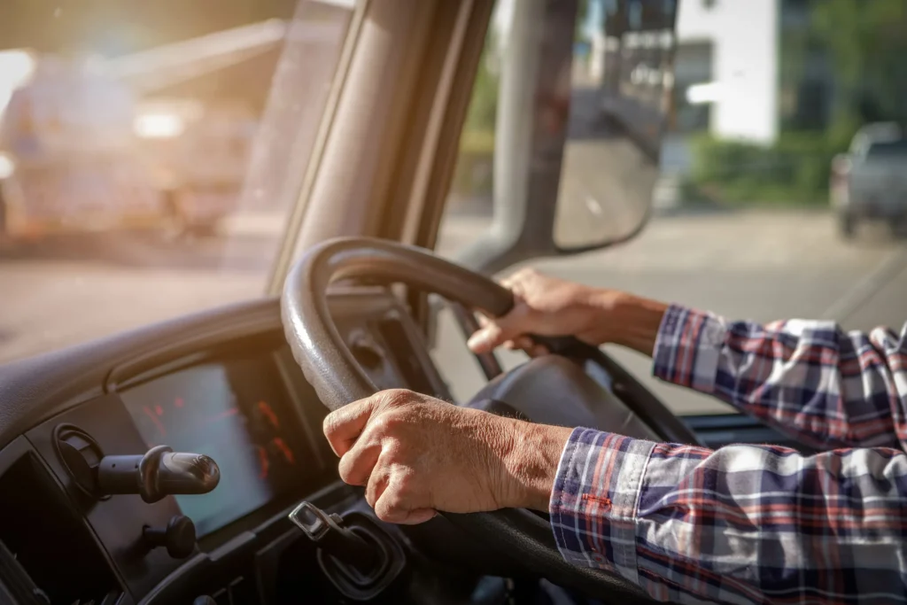 A truck driver's arms with his hands on steering wheel.