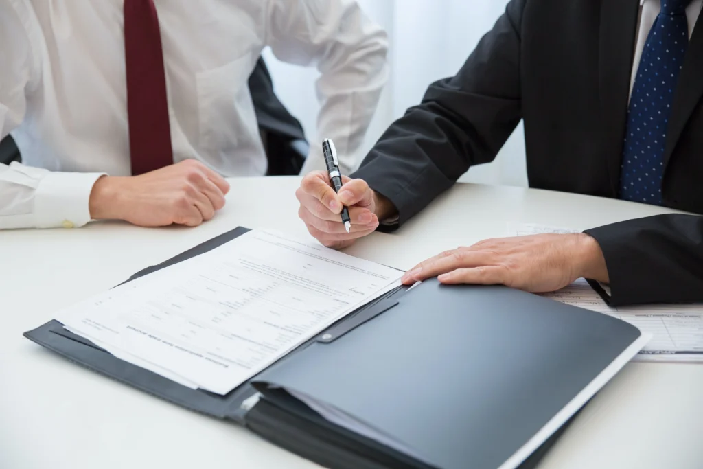 Two men setting at a desk while one signs some documents
