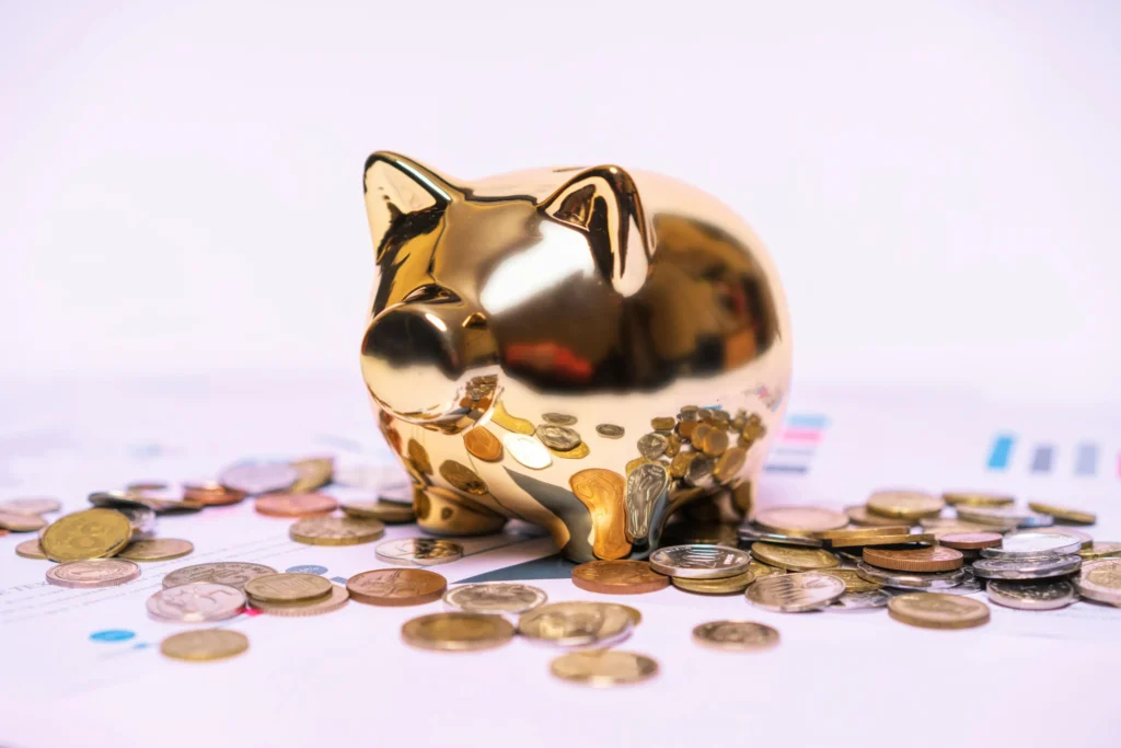Shiny gold piggy bank surrounded by scattered coins on financial documents, symbolizing savings and asset management.